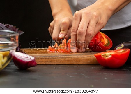 Cooking process, woman cutting tomatoes for aubergine paste from stocked eggplants