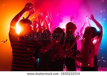 Festive. A crowd of people in silhouette raises their hands, dancing on dancefloor on neon light background. Night life, club, music, dance, motion, youth. Bright colors and moving girls and boys.