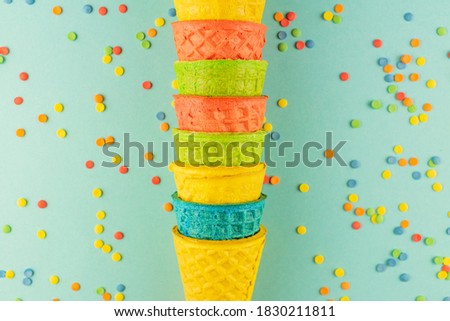 bright multicolored ice-cream waffle cones on blue background with scattered confetti sugar sprinkles.