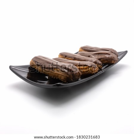 Five chocolate-coated eclairs on a rectangular black platter. Confectionery  lie in a row. Angle view. Isolated over white background.