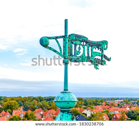 Old copper wind vane with green patina, shaped like a dragons head, mounted on the top of a building.