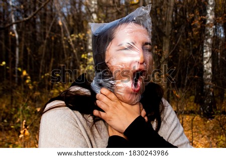 Portrait of a woman with a plastic bag on her head with an open mouth. Woman gasps with plastic bag on her face. Concept Stop using the plastic bag, plastic will kill you. Claustrophobia, fear. Royalty-Free Stock Photo #1830243986