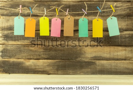 Eight price tags in different colors with space for text. Tags and inscriptions for text on a wooden background. The labels are hung on a rope with multi-colored clothespins
