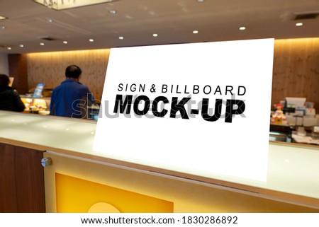 Mock up blank signboard stand with clipping path placed on wooden counter bar at food court, blurred people in background, empty space for insert text for announcement or information promotion