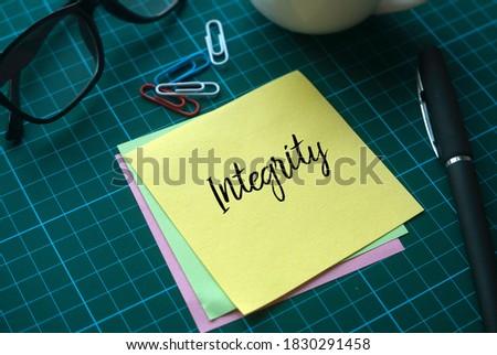 Selective focus of a cup of coffee, paper clips, glasses and memo notes written with Integrity on green square background.