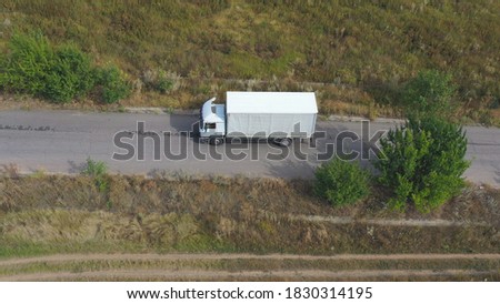 Aerial shot of truck with cargo trailer driving on road and transporting goods. Flying over delivery lorry moving along highway in countryside. Industrial car riding to destination. Logistic concept.