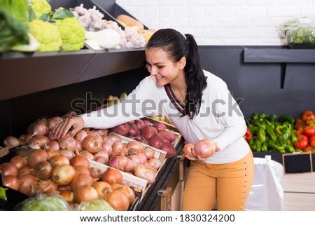 Smiling young woman customer examining various onions in grocery shop