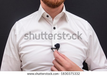 A man dressing in white shirt holding small lavalier microphone	