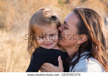 mom hugs and kisses her daughter in nature.