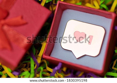 Like symbol in red gift box. Like sign heart button, symbol with heart and one digit. Social media network marketing. Multicolored tinsel background.