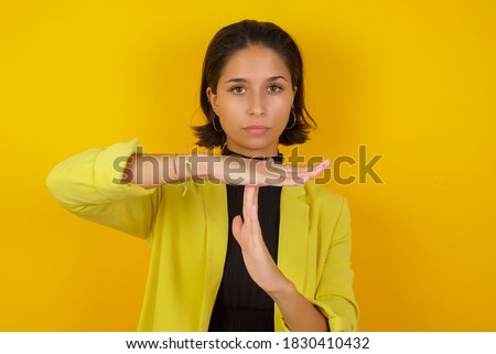 Young businesswoman wearing casual turtleneck sweater and jacket being upset showing a timeout gesture, needs stop, asks time for rest after hard work, demonstrates break hand sign Royalty-Free Stock Photo #1830410432
