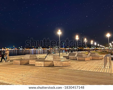 Night  promenade at pier  city light blurred sea water reflection people walk and relaxing starry blue sky wooden bench in Tallinn Estonia travel to Europe