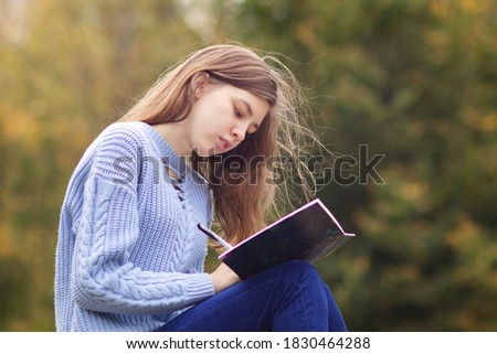 Young beautiful woman, teenager student is studying outdoors in park writing in notebook , with serious concentrated look, doing homework Royalty-Free Stock Photo #1830464288