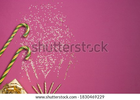 Candles are burning with golden confetti, gift box, candy cane. Festive, Christmas and New Year composition on a pink background. Horizontal orientation, top view. Copy space