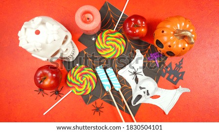Happy Halloween Trick or Treat theme background with candy and lollipops, skull and pumpkin on textured orange background. Top view blog hero header creative composition flat lay.