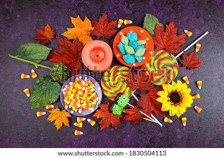 Happy Halloween Trick or Treat theme desktop with candy and lollipops, autumn leaves on stylish purple textured background. Top view blog hero header creative composition flat lay.
