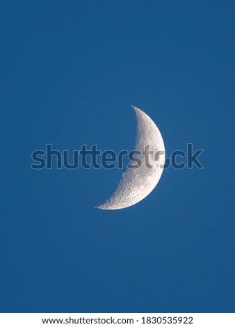 A waxing Crescent Moon in the blue sky with visible craters, mountains and lunar mare