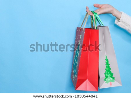 bags on blue background
Red and gray bags with a picture of a Christmas tree in a woman's hand on the right on a blue background and with a place for text on the left, close-up side view.