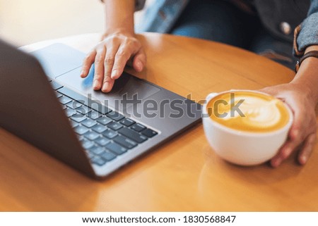 Closeup image of a woman working and touching on laptop computer touchpad while drinking coffee