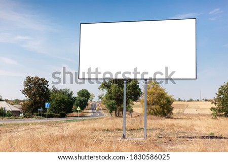 Empty billboard for advertising poster near asphalting road and village. Background of blue sky and beautiful nature.
