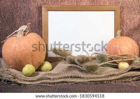 Portrait empty wooden frame mockup with pumpkins, yellow apples and dry grass on sackcloth. Brown background. Thanksgiving, Halloween concept. 

