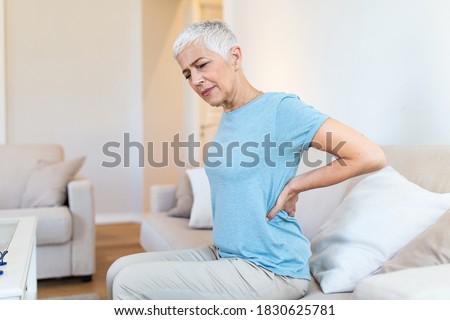 Upset mature middle aged woman feels back pain massaging aching muscles 