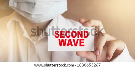 Second wave text on white card. Warning sign in doctor's hand. Second wave of covid-19 virus. Healthcare concept.