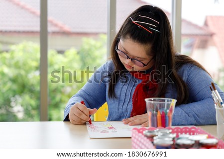 Girl with Down's syndrome drawing picture with crayon in art class. Concept disabled kid learning.