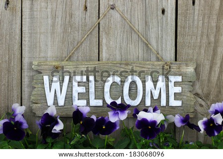 Wood welcome sign with purple flowers (pansies) hanging on wood background