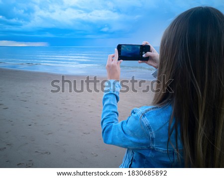 beautiful alone girl on the beach. Girl looking at stormy sea and taking a picture with smarphone. The spectacular Storm with rain Is Coming in Estonia. Baltic sea