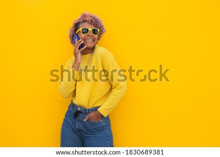 young afro american girl with mobile phone on the street outdoors and yellow background