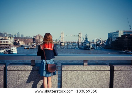 A young woman is standing on London bridge and admiring the skyline and the river Thames