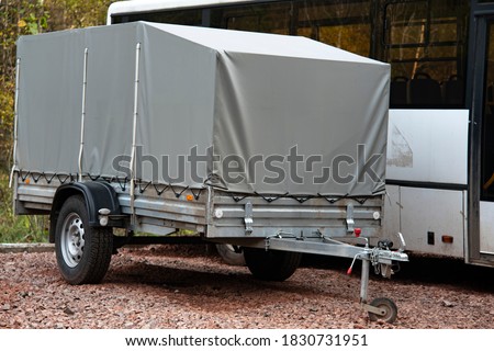 A car trailer covered with a gray tarpaulin in an unpaved parking lot. Royalty-Free Stock Photo #1830731951