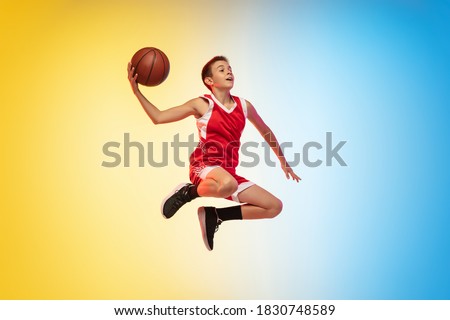 In fly. Full length portrait of young basketball player in uniform on gradient studio background. Teenager confident posing with ball. Concept of sport, movement, healthy lifestyle, ad, action, motion