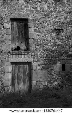 Old wooden door and window of a stone wall facade of a barn in Brittany (North of France, Black and white picture). 