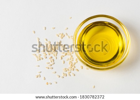Sesame oil in a glass bowl and sesame seeds on a white background, top view Royalty-Free Stock Photo #1830782372