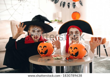 Cute little kids with pumpkin candy buckets wearing Halloween costumes at home