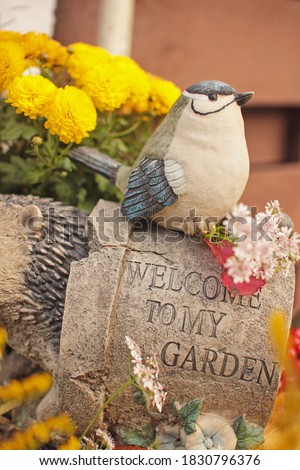 ceramic garden figure of a little bird, sitting on a flower pot, inscription welcome to my garden.Picture in fall style or spirit.Beautiful autumn composition with gardening decor and flowers.