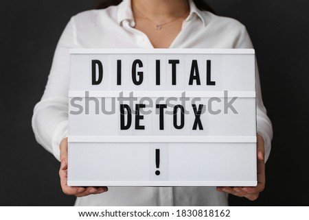 Woman holding lightbox with phrase DIGITAL DETOX on black background, closeup