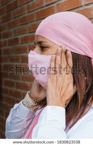 Woman putting on a pink mask and wearing a pink scarf from the breast cancer. Lifestyle. health