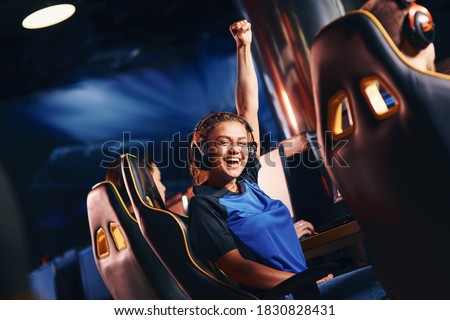 Young happy mixed race girl, female cybersport gamer raising hand up and smiling at camera while participating in eSport tournament Royalty-Free Stock Photo #1830828431