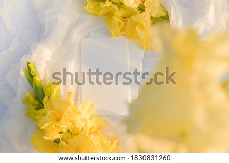 Blank paper card with copy space . Yellow gladiolus flower on white textile background. Styled stock photography for display your design, lettering, font, illustration, wedding stationary. Flat lay