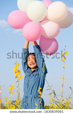 Happy young girl hold balloon at yeloow flower park with blue sky.