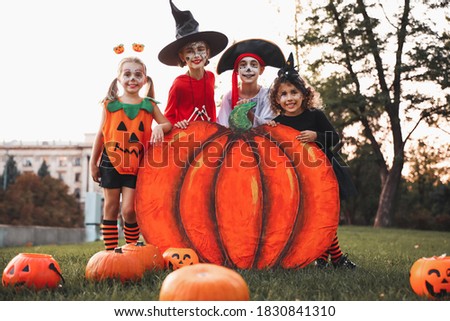 Cute little kids with decorative pumpkin wearing Halloween costumes in park