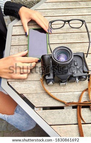 Woman using modern smartphone and retro vintage film camera.