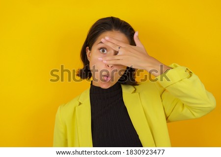 Young businesswoman wearing casual turtleneck sweater and jacket peeking in shock covering face and eyes with hand, looking through fingers with embarrassed expression.