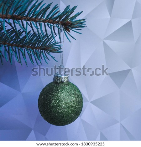 round shiny green Christmas toy hanging on a Christmas tree branch on a blue background
