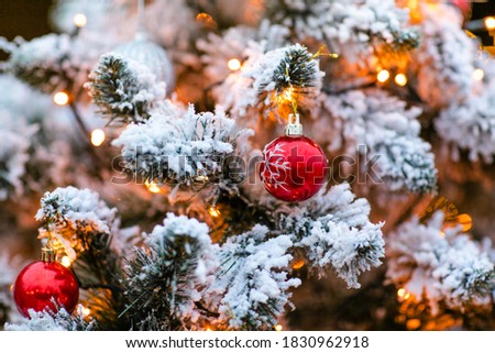 Fir tree decorated with snow and toy red glass ball and light bulbs for Christmas and New Year celebration