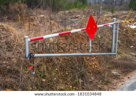 A security swinging gate with a red sign and locks is open on a deserted road 
