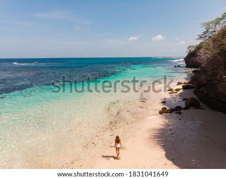  Flying high above unrecognizable tourist girl exploring tropical island,  walking alone on amazing tropical white sand beach with torquise ocean. Tropical vacations concept